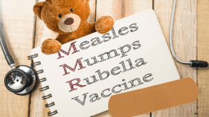 一只泰迪熊拿着一个记事本，上面写着:麻疹、腮腺炎、风疹、疫苗.